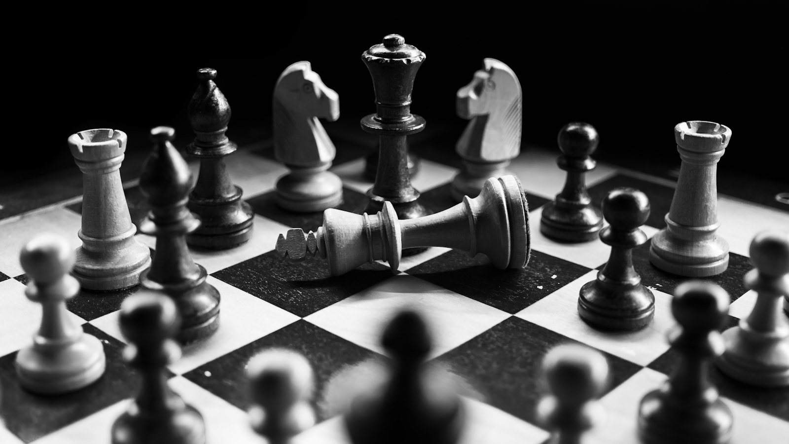 Black and white chess pieces with a fallen king